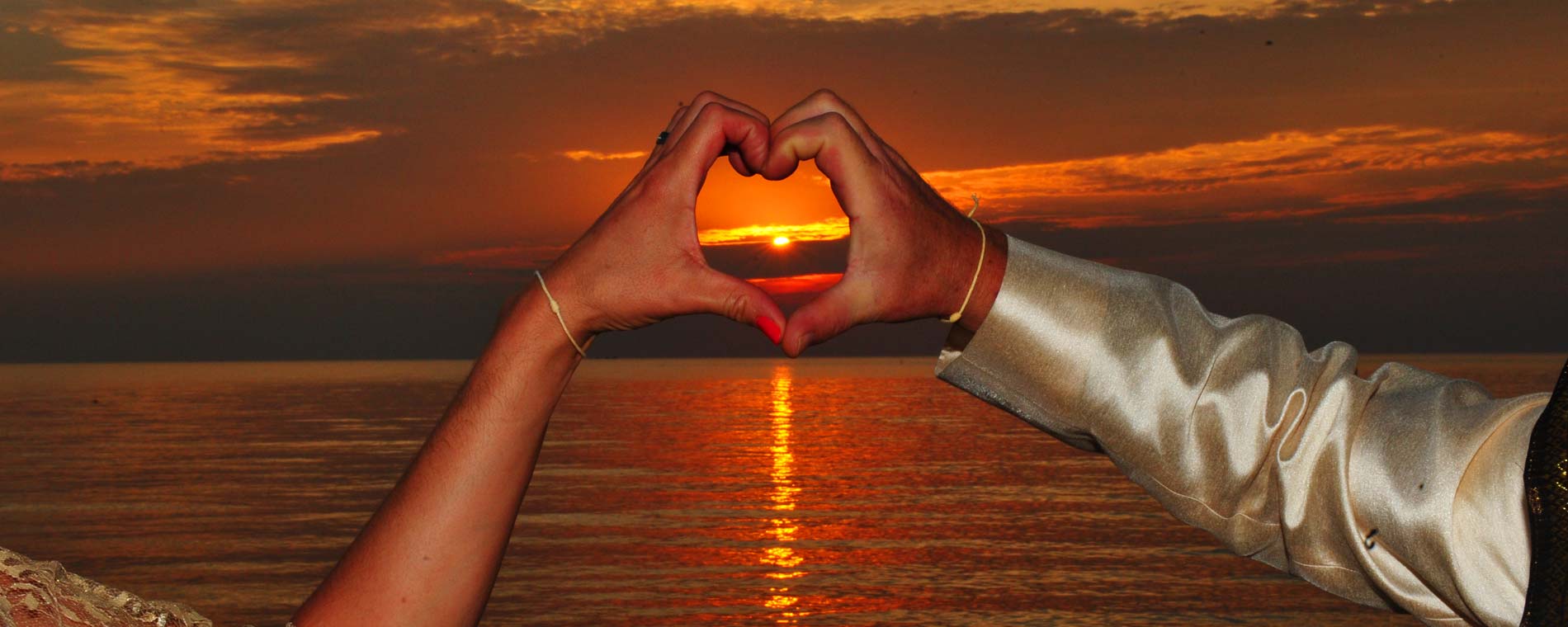 Ein Paar formt mit den Händen ein Herz vor dem Sonnenuntergang am Meer